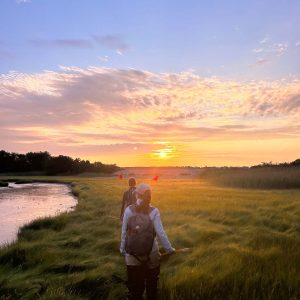 Two researchers walk through the salt marsh at sunrise.